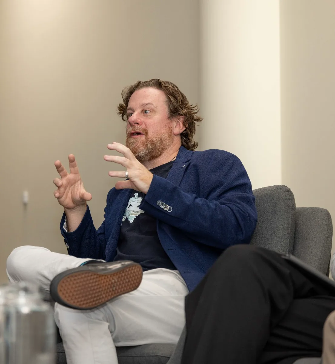 Simon Lowe in conversation, hands raised mid-sentence in an armchair