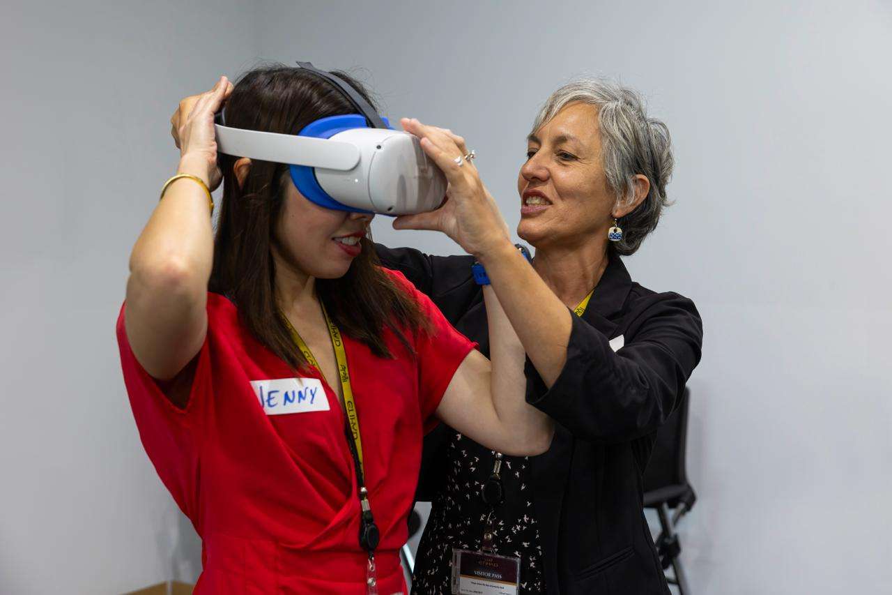 A facilitator fits a VR headset onto a participant wearing an Etihad visitor pass, part of PTR's immersive training workshop with Etihad Airways in February 2024.