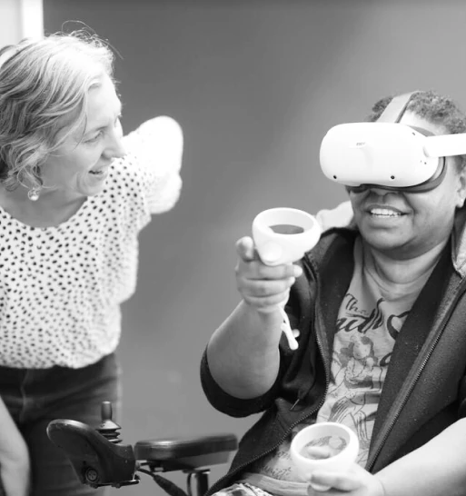 A person wearing a Meta Quest VR headset smiles and holds out a cup while another looks on, part of Mayo Clinic's VR nursing training scenario.