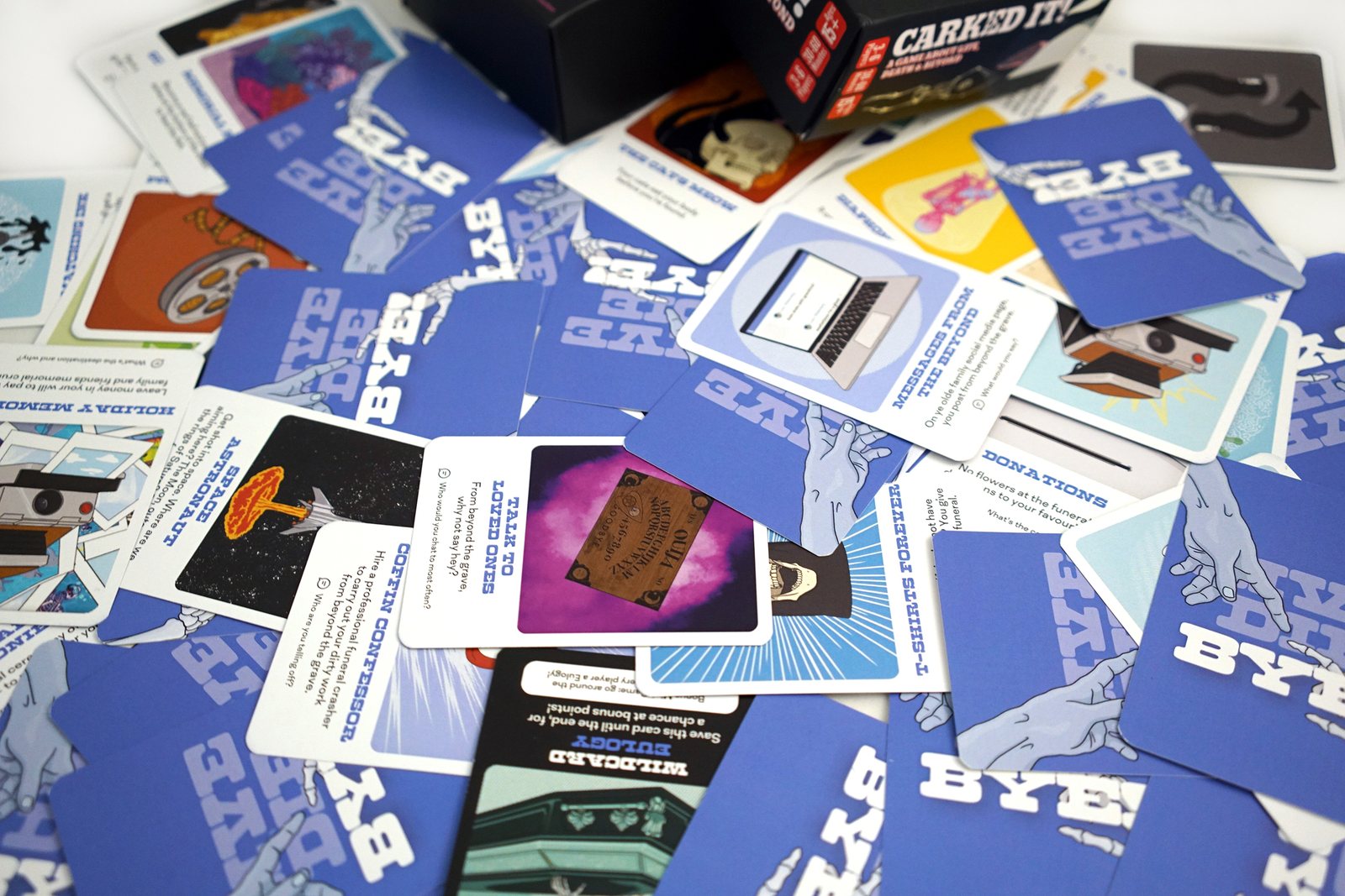 Blue cards from the BYE deck scattered face up, with titles about messages from the beyond and coffin confessions.