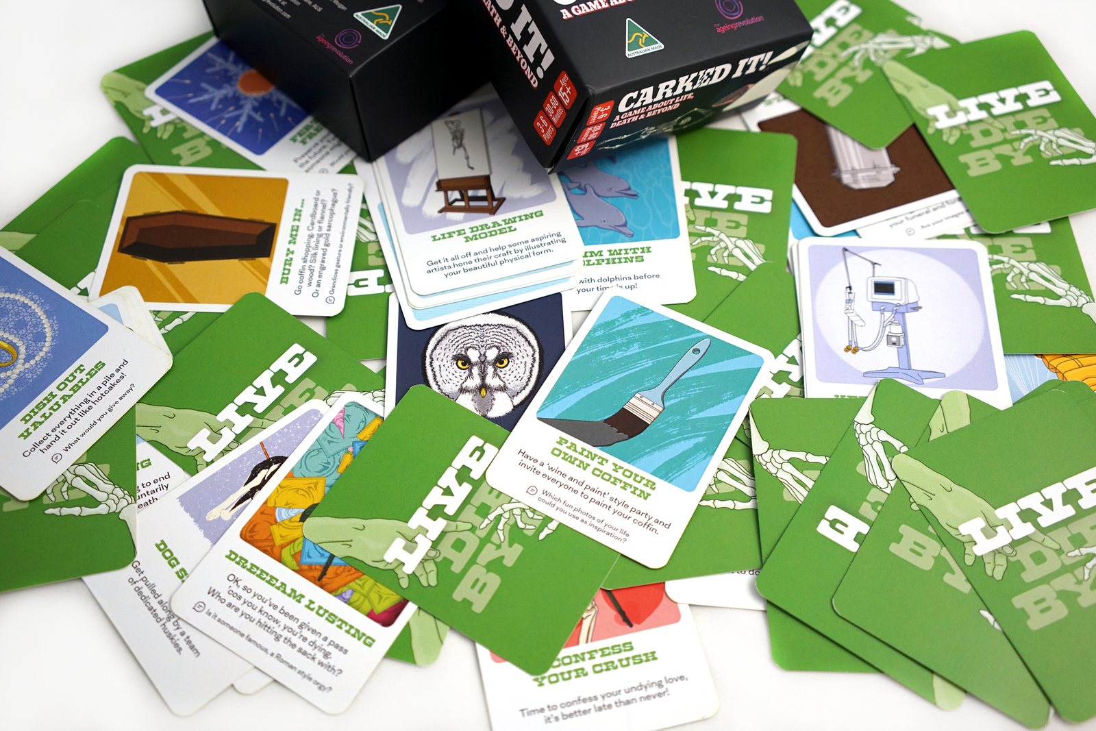 Green cards from the LIVE deck spread face up, illustrated with a life drawing easel, a paintbrush on a coffin and a swim with something wild.