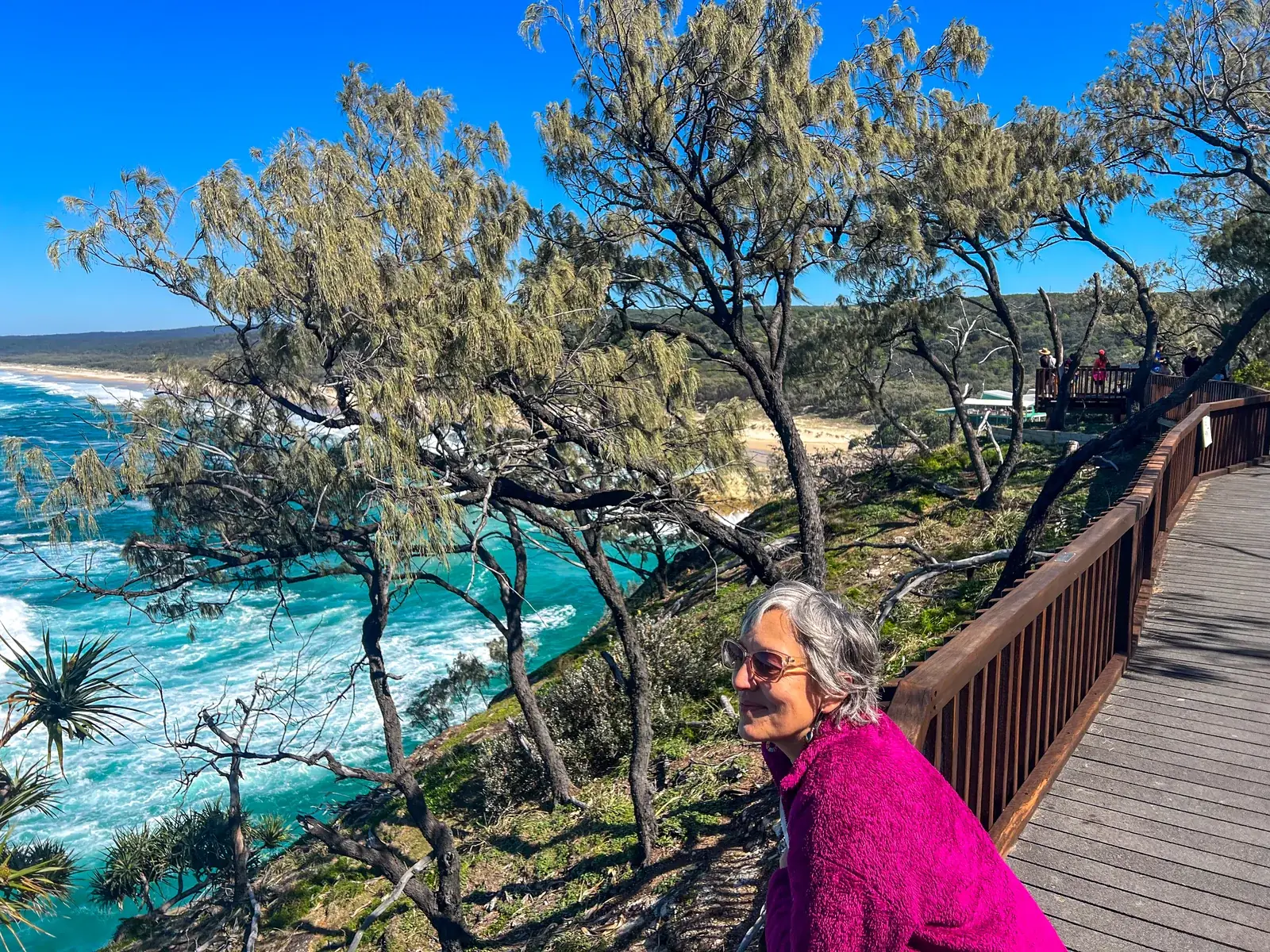 Leonie Sanderson at a coastal lookout, casuarinas and a turquoise bay behind her.