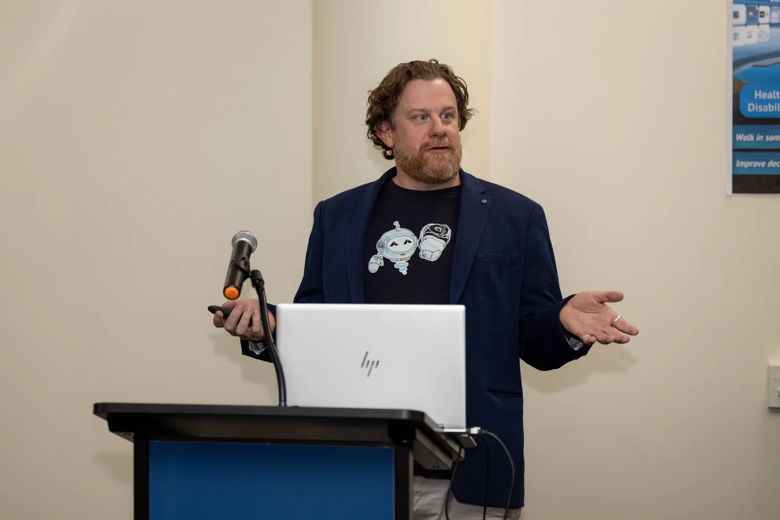 Simon Lowe at a lectern, mid-sentence beside a laptop.