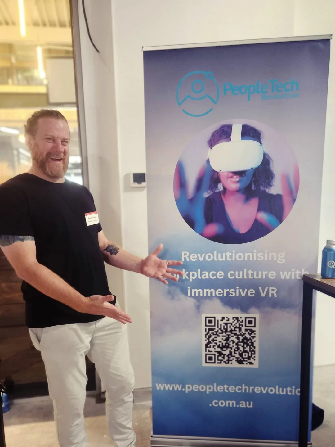 PTR's CEO Simon Lowe gesturing toward a PTR pull-up banner reading 'Revolutionising workplace culture with immersive VR' at a technology council event.